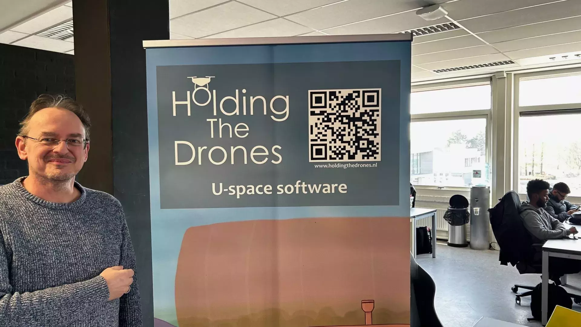 Eigenaar Elie staat naast een bord met het logo van Holding the Drones