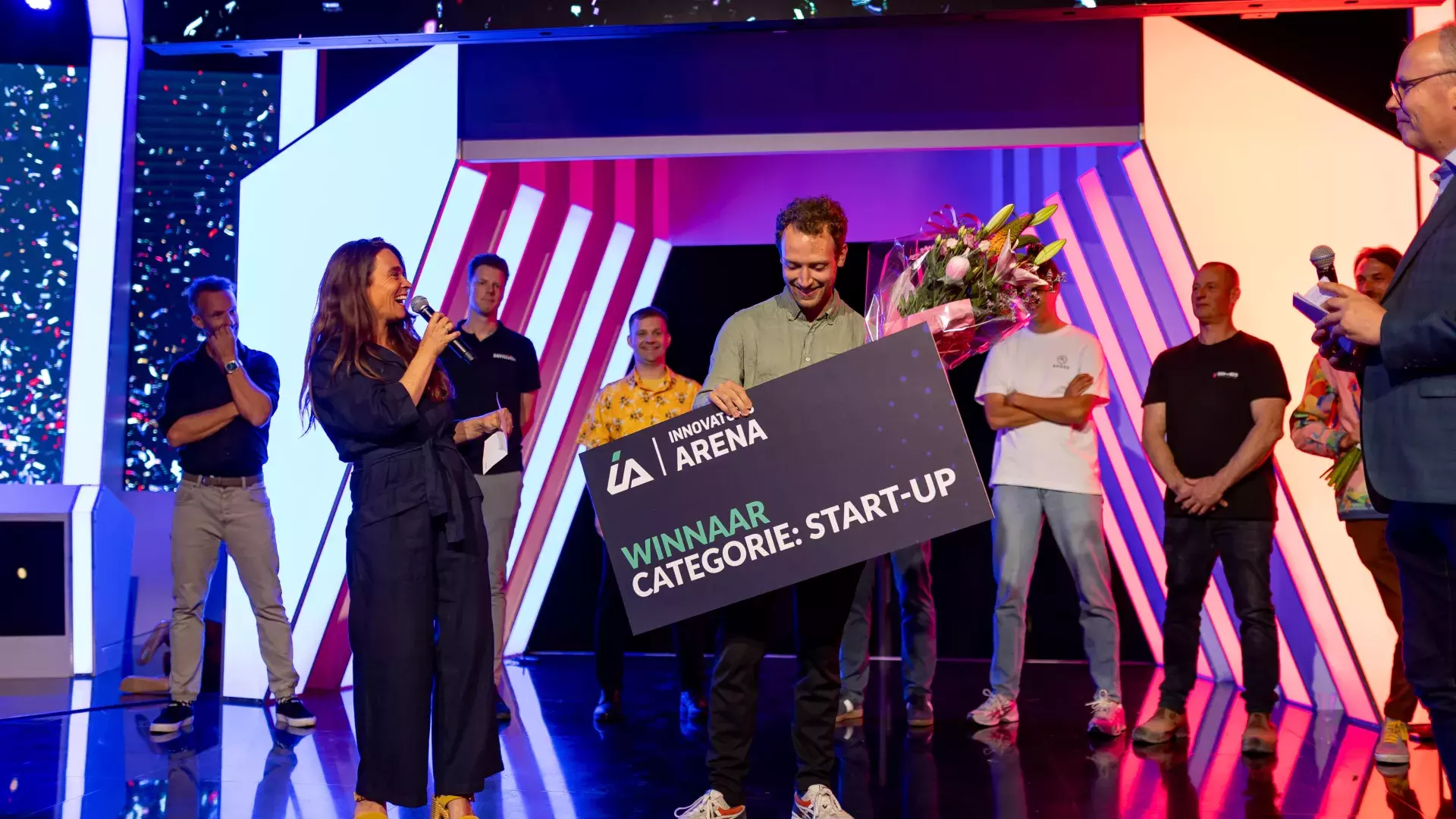 foto van Jacob van Alderli met de winnaarscheque in zijn hand. De presentatrice van het event staat naast hem, lacht en klapt.